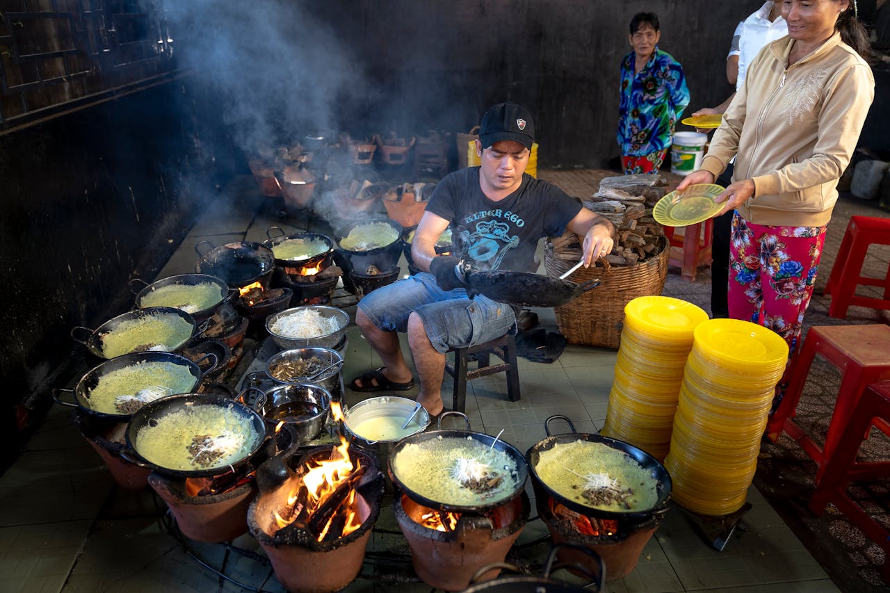 Mastering the First Impression: Your intriguing post title goes here A street vendor cooking multiple Vietnamese pancakes over open flames in a bustling market setting.