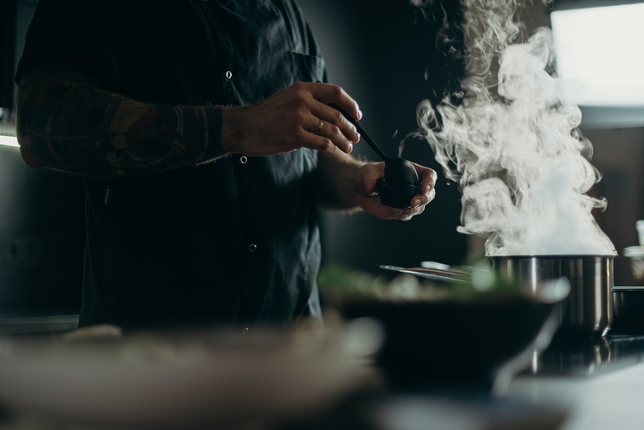 A chef carefully prepares a steamy dish in a professional kitchen setting.
